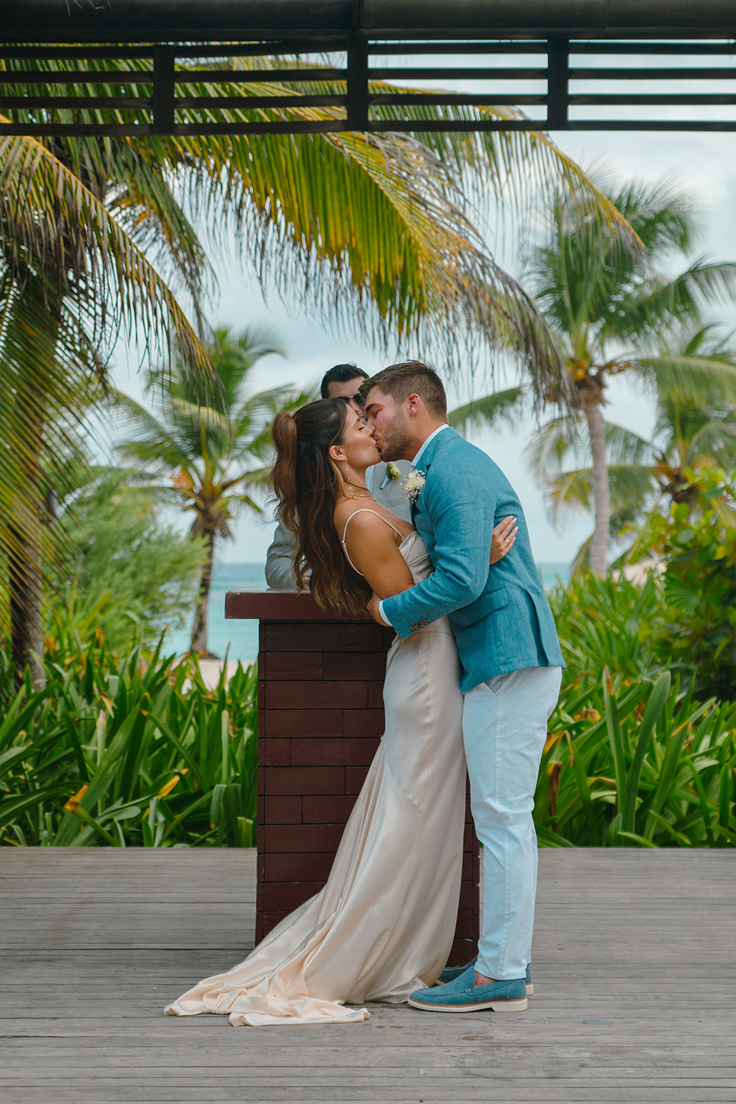 Bride and groom first kiss with palm trees and ocean in background