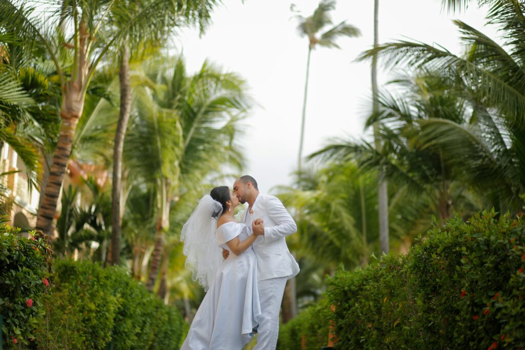 Couple in all white wedding attire kissing underneath palm trees in mexico