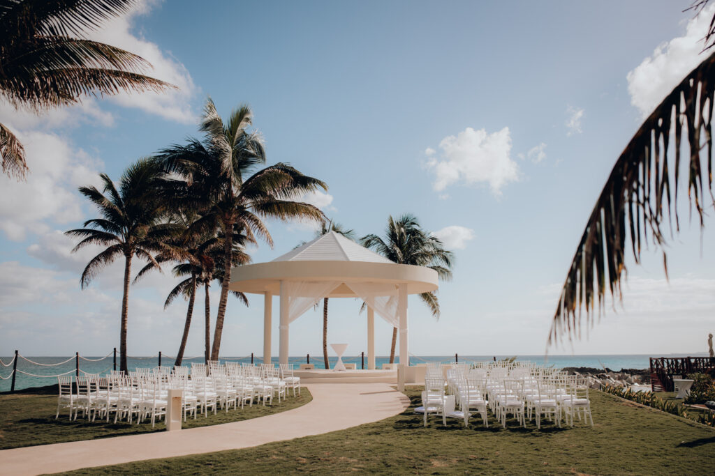 wedding ceremony space at hyatt ziva cancun with white gazebo and white chairs in front of ocean with palm trees