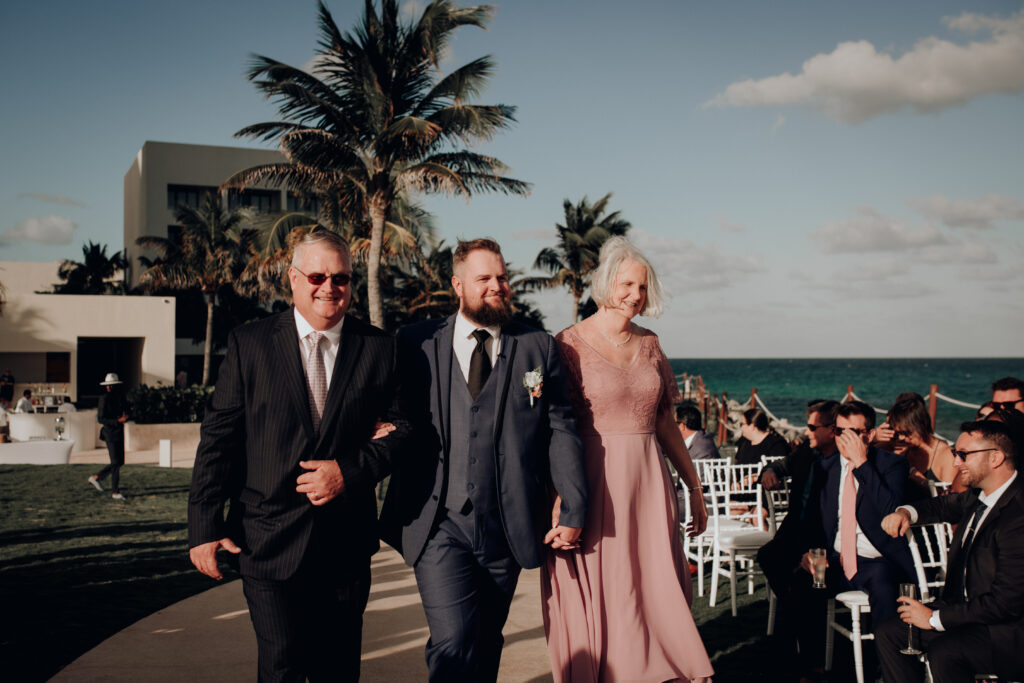 groom walking down aisle with both parents during wedding ceremony at hyatt ziva cancun