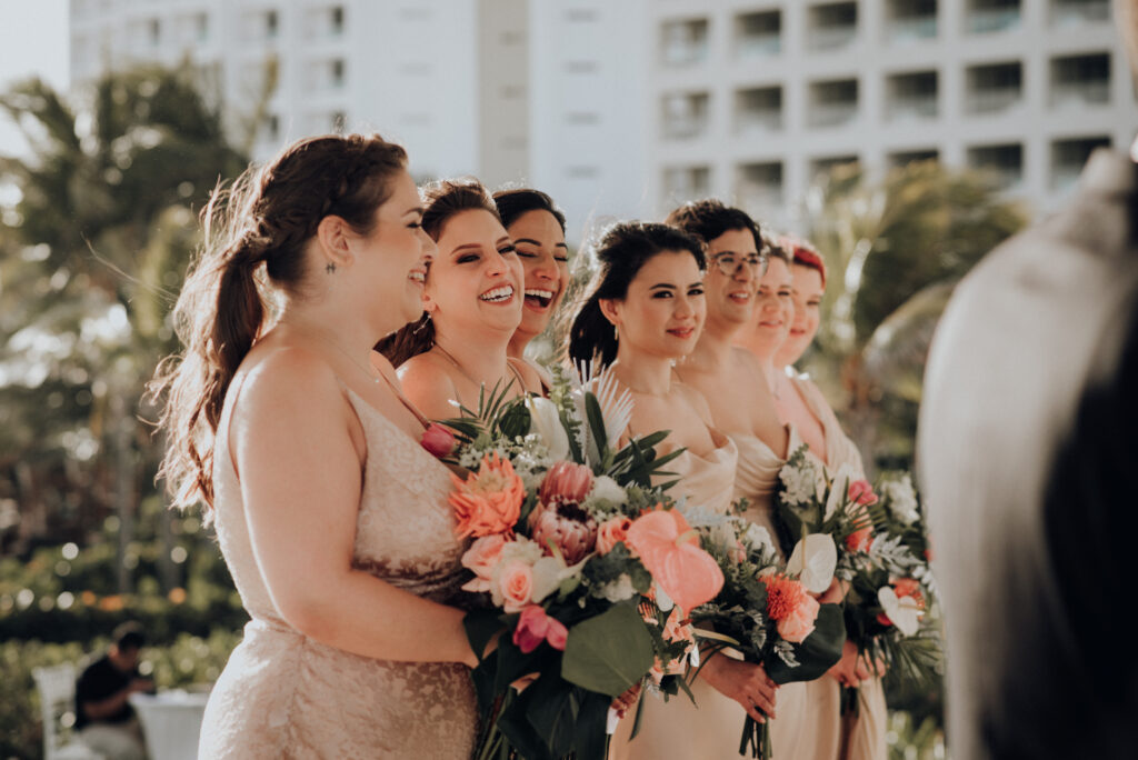 bridesmaids wearing gold dresses and carrying tropical bouquets laughing during wedding ceremony 