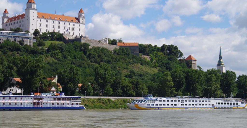 Two river cruise ships docked in Bratislava, Slovakia in front of the castle along a Danube river cruise itinerary.