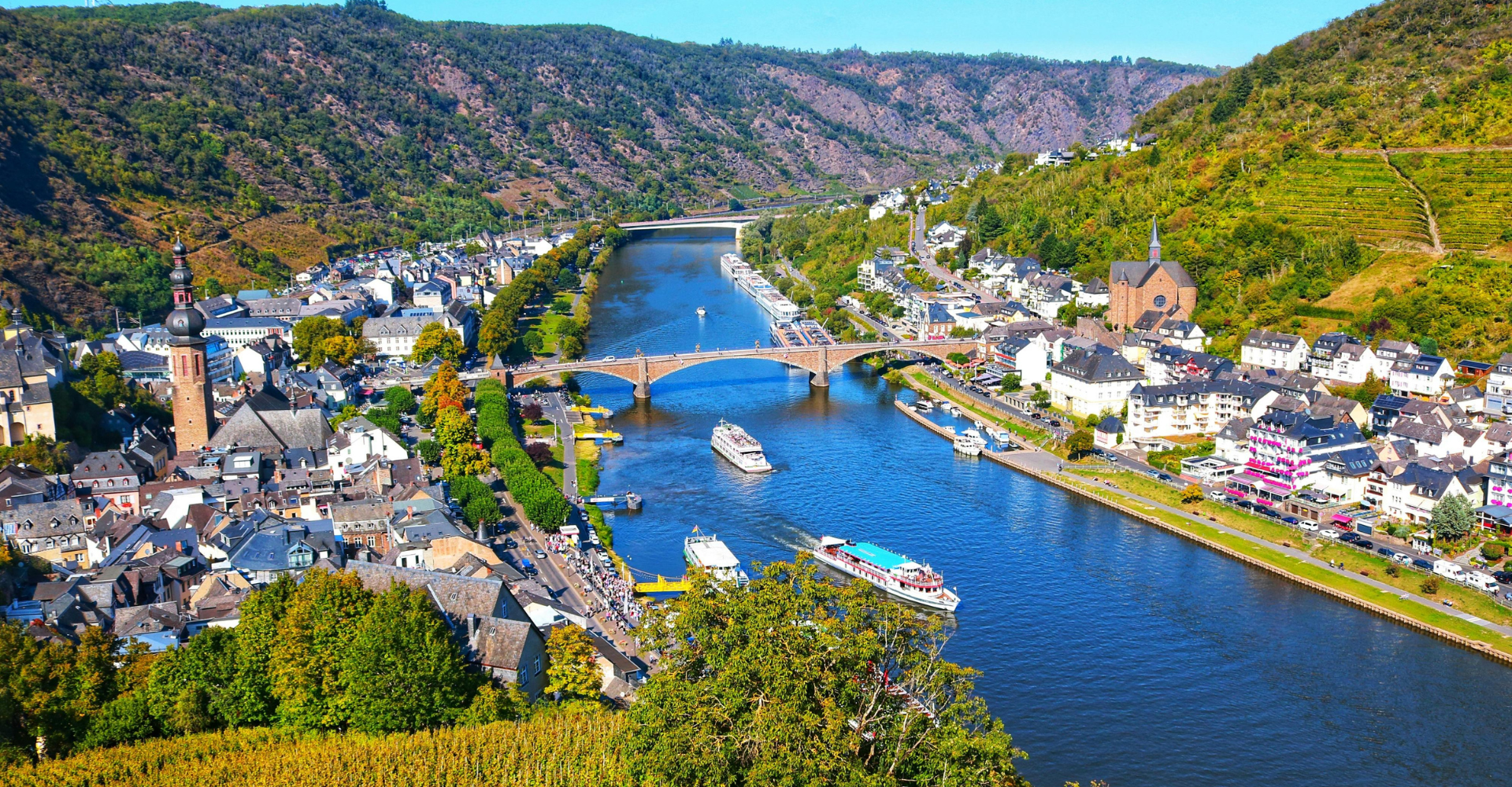 Multiple river cruise ships sailing through scenic European towns surrounded by lush landscapes during a European river cruise.
