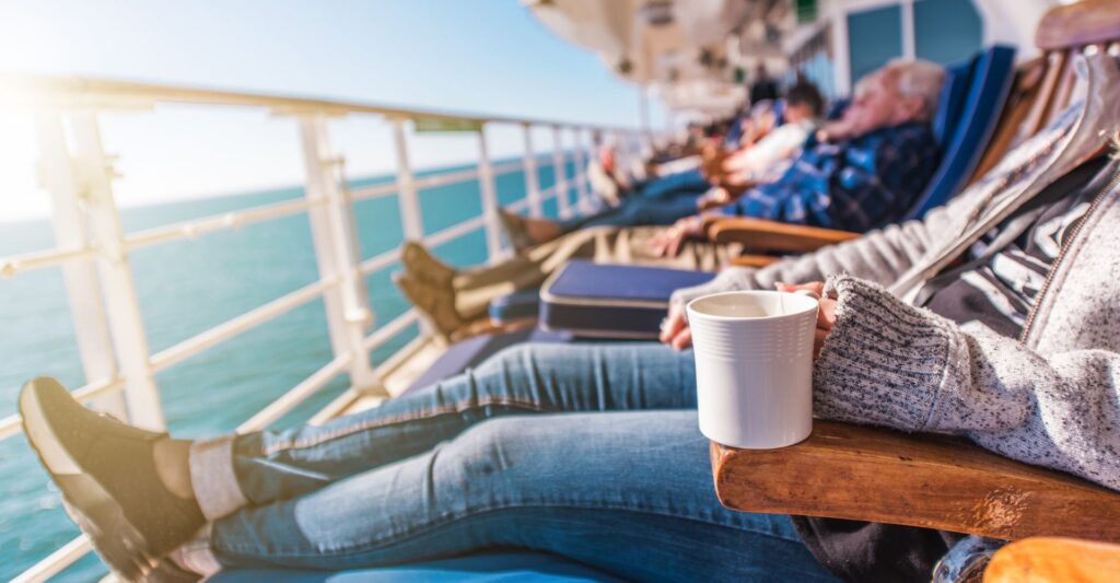 Travelers relaxing on a river cruise ship sundeck enjoying coffee and scenic views, showcasing comfortable river cruise attire and the relaxed experience of what to wear on a river cruise.